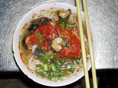 Bát bún ốc với cà chua, hành và thịt ốc